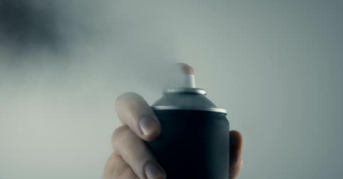 Hand holding spray paint can sprays into camera